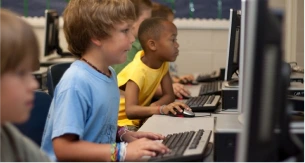 Des enfants concentrés devant des ordinateurs dans une salle de classe, illustrant l'apprentissage des nouvelles technologies et le développement des compétences numériques dès le jeune âge